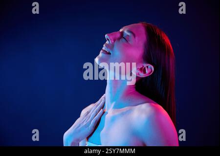 Vista laterale. Ritratto di una giovane donna in interni con illuminazione al neon. Foto Stock