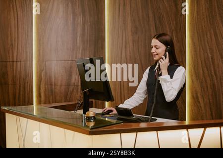 Un'ampia gamma di giovani donne adulte che guardano lo schermo del computer e rispondono alle chiamate mentre lavorano come receptionist in hotel Foto Stock
