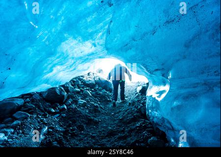 Una persona da dietro che esce da una grotta di ghiaccio blu nel ghiacciaio Vatnajokull, Islanda Foto Stock