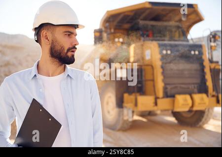 Un bell'uomo in uniforme lavora in cava di giorno. Con dumper da trasporto. Foto Stock