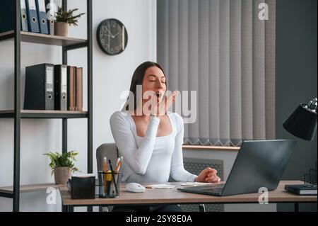 Una donna stanca sbadiglia. Giovane donna bella lavoratrice d'ufficio in vestiti bianchi è in ufficio. Foto Stock