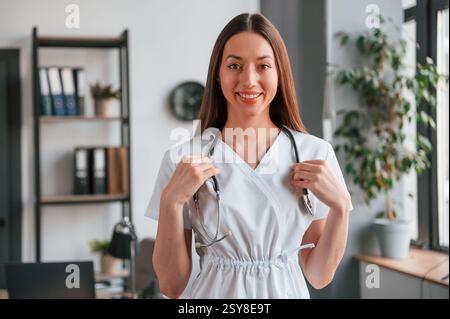 Ritratto di giovane bella dottoressa donna in cappotto bianco che è in ufficio. Foto Stock