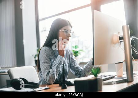 Una giovane designer donna è nell'ufficio moderno e lavora con il computer. Foto Stock