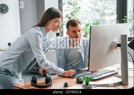 L'uomo è seduto, la donna è in piedi. Tramite pc. Due giovani designer stanno lavorando insieme in ufficio. Foto Stock