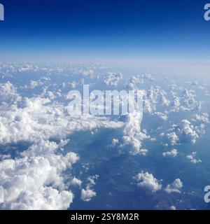 Vista aerea delle nuvole dalla finestra di un aeroplano con cielo blu brillante sopra e copertura delle nuvole di cumulus sparse sotto Foto Stock