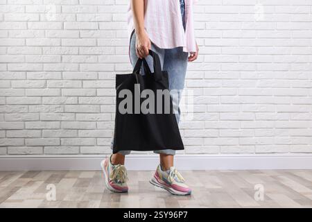 Donna con sacchetto nero vuoto vicino a un muro di mattoni bianchi, primo piano. Mockup per il design Foto Stock