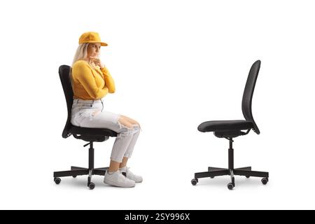 Giovane donna seduta su una sedia da ufficio e che guarda una sedia vuota isolata su sfondo bianco Foto Stock