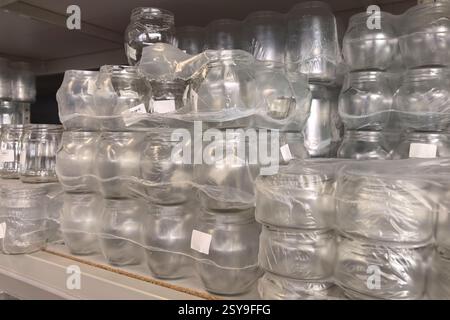 Numerosi vasetti in vetro trasparente sono disposti in file meticolosi sullo scaffale di un negozio. I barattoli, avvolti in plastica, riflettono la luce mentre aspettano di essere acquistati Foto Stock