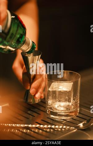 Mano del barista che versa alcol a jigger. Bartending e mixology Foto Stock