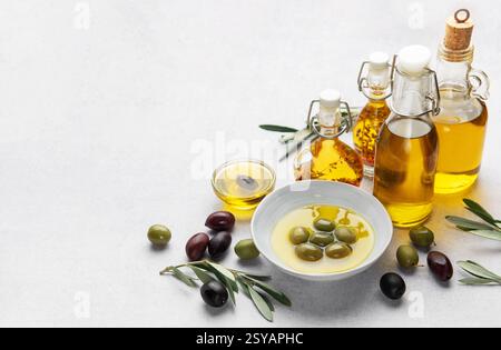 Varie bottiglie di vetro e ciotole di olio d'oliva sono accompagnate da olive e rami d'oliva, creando una scena culinaria rustica Foto Stock