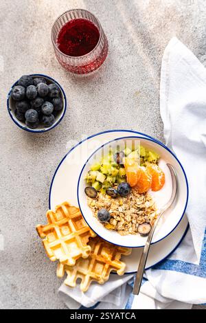 Vista dall'alto di una sana colazione a buffet con yogurt con muesli, kiwi freschi, fette d'arancia, mirtilli, cialde, e un bicchiere di succo Foto Stock