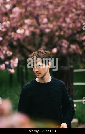 Un giovane ma viene catturato in una posa serena e contemplativa sullo sfondo di lussureggianti fiori di ciliegio e tulipani durante la primavera. La vivace flora prov Foto Stock