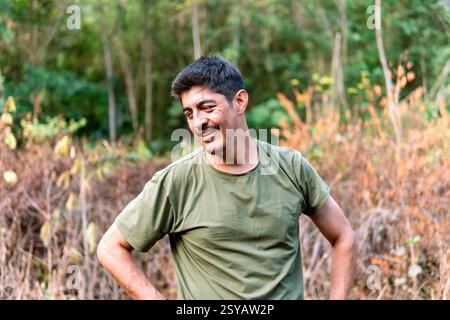 Un uomo colombiano di mezza età si prende una pausa gioiosa in mezzo al lavoro agricolo nella campagna rurale colombiana, circondato da una vegetazione lussureggiante e sotto la dolce giornata Foto Stock