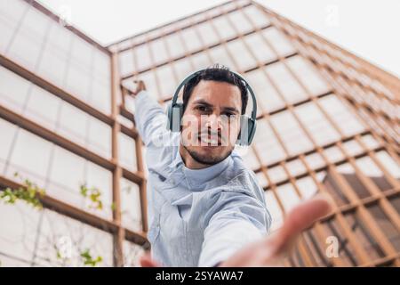 Un giovane cubano con una camicia azzurra, indossa le cuffie, indossa una posa da ballo dinamica. Sorride con fiducia in uno sfondo di storia moderna della città Foto Stock