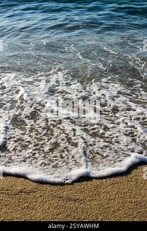 Vista ravvicinata delle onde morbide che scivolano su una spiaggia sabbiosa, catturando il movimento sereno dell'acqua e della schiuma sotto la luce del sole. Perfetto per la natura o per il re Foto Stock
