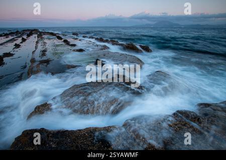 Tranquillo tramonto sulla costa rocciosa di Tarifa, Cadice. Le onde si infrangono dolcemente sulle rocce accidentate, creando un bellissimo paesaggio marino nelle soffici serali Foto Stock