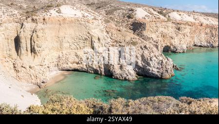 Le scogliere mozzafiato si affacciano sulle tranquille acque azzurre di Tsigrado sull'isola di Milos, in Grecia. La spiaggia incontaminata e il terreno accidentato creano una fuga perfetta Foto Stock