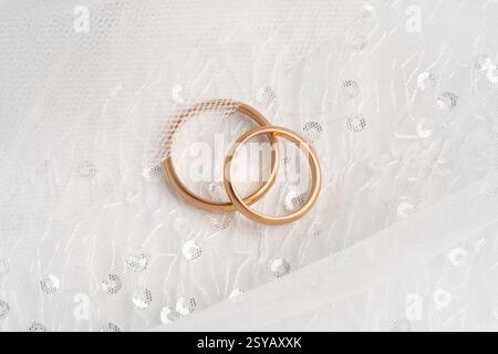 Primo piano di due fedi nuziali intrecciate in oro rosa su un delicato tessuto in pizzo bianco, a simboleggiare l'amore e l'impegno eterni. Foto Stock