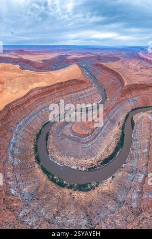Una splendida vista aerea cattura un fiume serpentino che si snoda attraverso formazioni rocciose a strati in un aspro paesaggio desertico, che mostra arte e natura Foto Stock