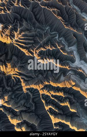 Foto aerea che cattura le texture dorate del deserto e gli intricati motivi di Caineville Mesa, Utah. La luce del sole proietta ombre spettacolari, evidenziando la r Foto Stock