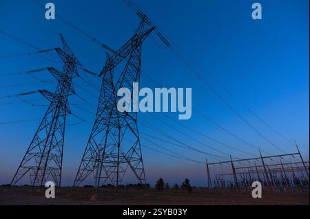 Le maestose linee elettriche ad alta tensione si estendono su un sereno cielo serale, con sagome che si stagliano contro la luce che svanisce, simboleggiando le infrastrutture elettriche e la Foto Stock