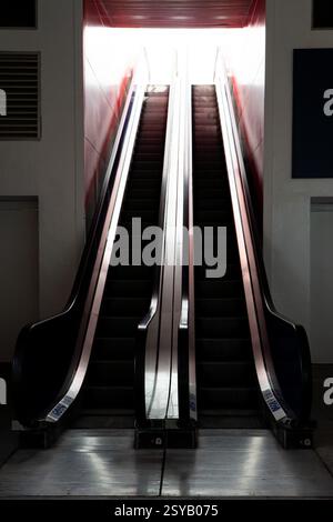 Una scala mobile molto illuminata catturata tra i momenti di utilizzo, che crea un senso di movimento in un'elegante e moderna architettura urbana. Foto Stock