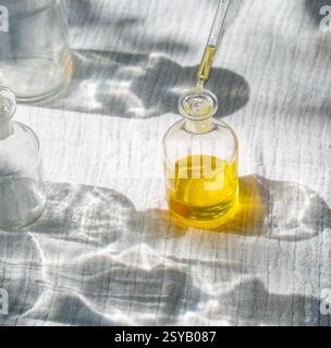Una bottiglia di vetro riempita con olio naturale dorato si trova sotto la luce del sole, poiché una pipetta aggiunge più liquido. A base di piante come la calendula, la rosa, la lavanda Foto Stock