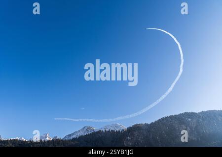 Un jet crea uno splendido giro in contrail attraverso un cielo blu brillante in un festival di mongolfiere del castello di Oex, lasciando un sentiero sopra una serena cuffia da neve Foto Stock