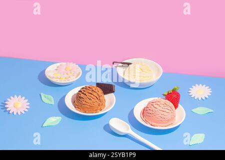 Quattro ciotole di gelato al gusto di vaniglia, cioccolato e fragola, disposte su uno sfondo rosa e blu diviso con fiori di carta decorativi e. Foto Stock