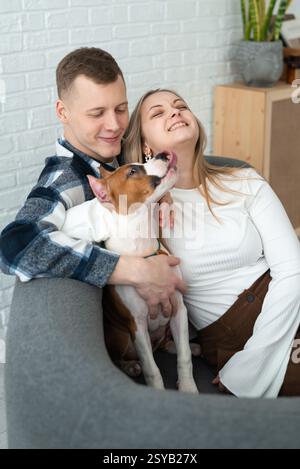 Un uomo e una donna gioiosi condividono un momento di amore con il loro cane bianco e marrone giocoso, seduto comodamente nella loro casa elegante e accogliente. Foto Stock