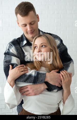 Un giovane uomo e una donna condividono un tenero abbraccio in una casa luminosa, che trasmette calore e vicinanza. La loro posa affettuosa e le loro espressioni gioiose ex Foto Stock
