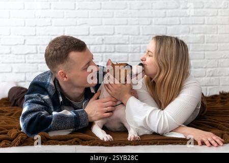 Un giovane uomo e una donna interagiscono amorevolmente con il loro cucciolo Staffordshire Terrier a casa, creando una scena sentita in un ambiente accogliente con un bianco Foto Stock