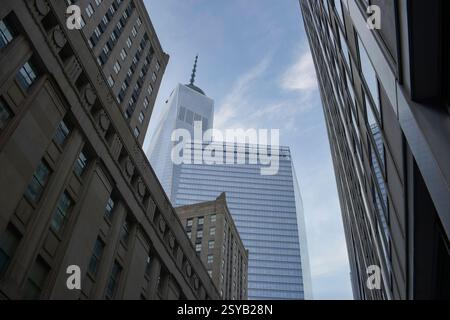 Un angolo verso l'alto cattura l'iconica silhouette del One World Trade Center tra gli edifici circostanti a Manhattan, contro un cielo blu. Foto Stock