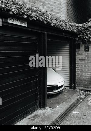 Un'elegante auto sportiva è parcheggiata in modo discreto in un garage con un cartello "No Parking". L'ambiente urbano di Londra presenta pareti in mattoni e fogliame per contrasto Foto Stock