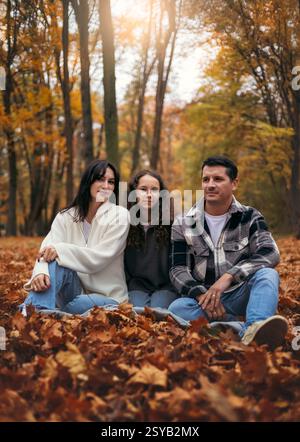 Una famiglia siede in mezzo a una foresta ricoperta di vibranti foglie autunnali. Il sole tramonta filtra tra tra gli alberi, creando una calda e pittoresca scena autunnale Foto Stock
