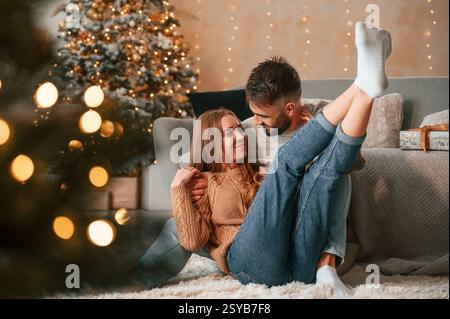 Seduti sul pavimento insieme. Una bella giovane coppia festeggia il nuovo anno a casa. Foto Stock