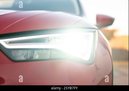 Primo piano del faro anteriore di un SUV rosso che si illumina di luce, mettendo in risalto il moderno design automobilistico e l'illuminazione potente, perfetto per i veicoli dinamici e futuristi Foto Stock