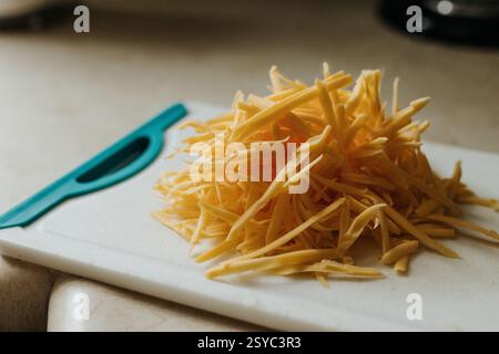 Un mucchio di formaggio cheddar appena grattugiato si trova sul tagliere Foto Stock