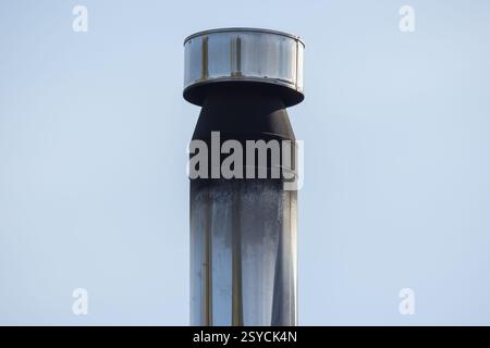 Vista panoramica di un tubo cilindrico in metallo lucido con cappuccio protettivo e parte superiore nero fumo sotto un cielo azzurro, per catturare l'industria e la risoluzione Сlose Foto Stock