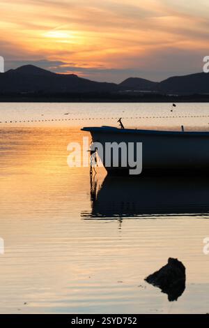 Barca ancorata al tramonto a Playa Honda, la Manga del Mar Menor, Cartagena, regione di Murcia, Spagna, con acque calme e cielo arancione riflesso Foto Stock