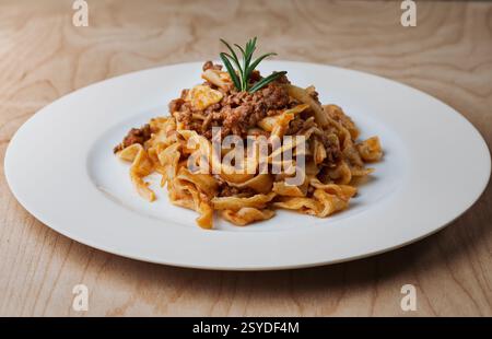 Tagliatelle fatte in casa con ricca salsa ragù, servite su un piatto bianco, classico cibo italiano Foto Stock