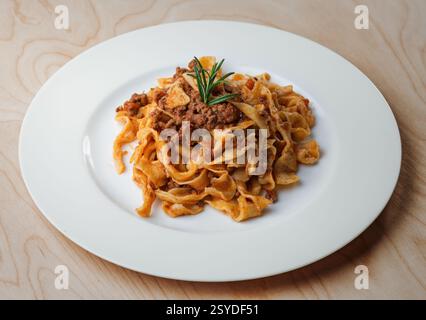 Tagliatelle fatte in casa con ricca salsa ragù, servite su un piatto bianco, classico cibo italiano Foto Stock
