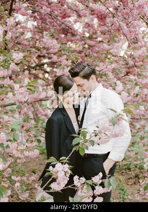 Una coppia gode di un momento tenero circondato da lussureggianti ciliegi rosa in fiore durante una splendida giornata primaverile. Foto Stock