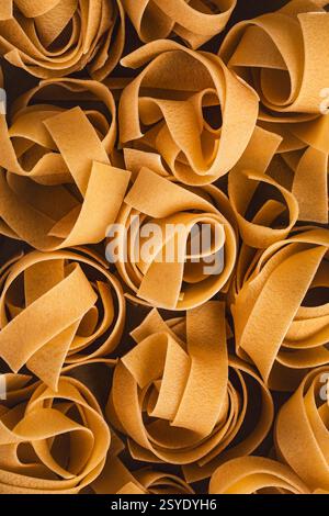 Primo piano di nidi di pappardelle secche che che mostrano gli ampi nastri dorati piatti disposti in formazioni ondulate. Foto Stock