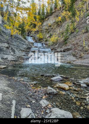Una cascata a più livelli scorre attraverso un aspro paesaggio roccioso, incorniciato da alberi d'autunno dorati. La cascata naturale crea una scena dinamica in una prospettiva remota Foto Stock