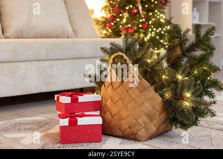 Cestino in vimini con rami di abeti e luci natalizie vicino alle confezioni regalo sul pavimento in interni Foto Stock