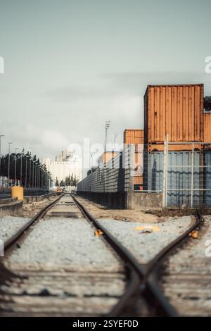 Un teleobiettivo verticale ad angolo basso di binari ferroviari che si dividono in due in un terminal merci industriale, circondato da contenitori di spedizione arancioni, Foto Stock