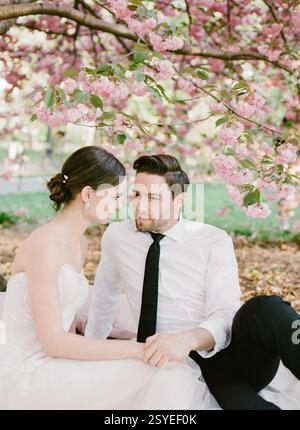 Una coppia condivide uno sguardo amorevole mentre si siede sotto i ciliegi rosa in una giornata di primavera assolata. Foto Stock