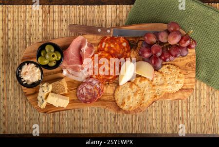Una tavola di legno con una varietà di cibi, tra cui cracker, formaggio, uva, olive e carne Foto Stock