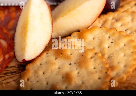 Una tavola di legno di cracker e una fetta di mela. I cracker si trovano su un asse di legno e la mela si trova sul lato sinistro della piastra Foto Stock